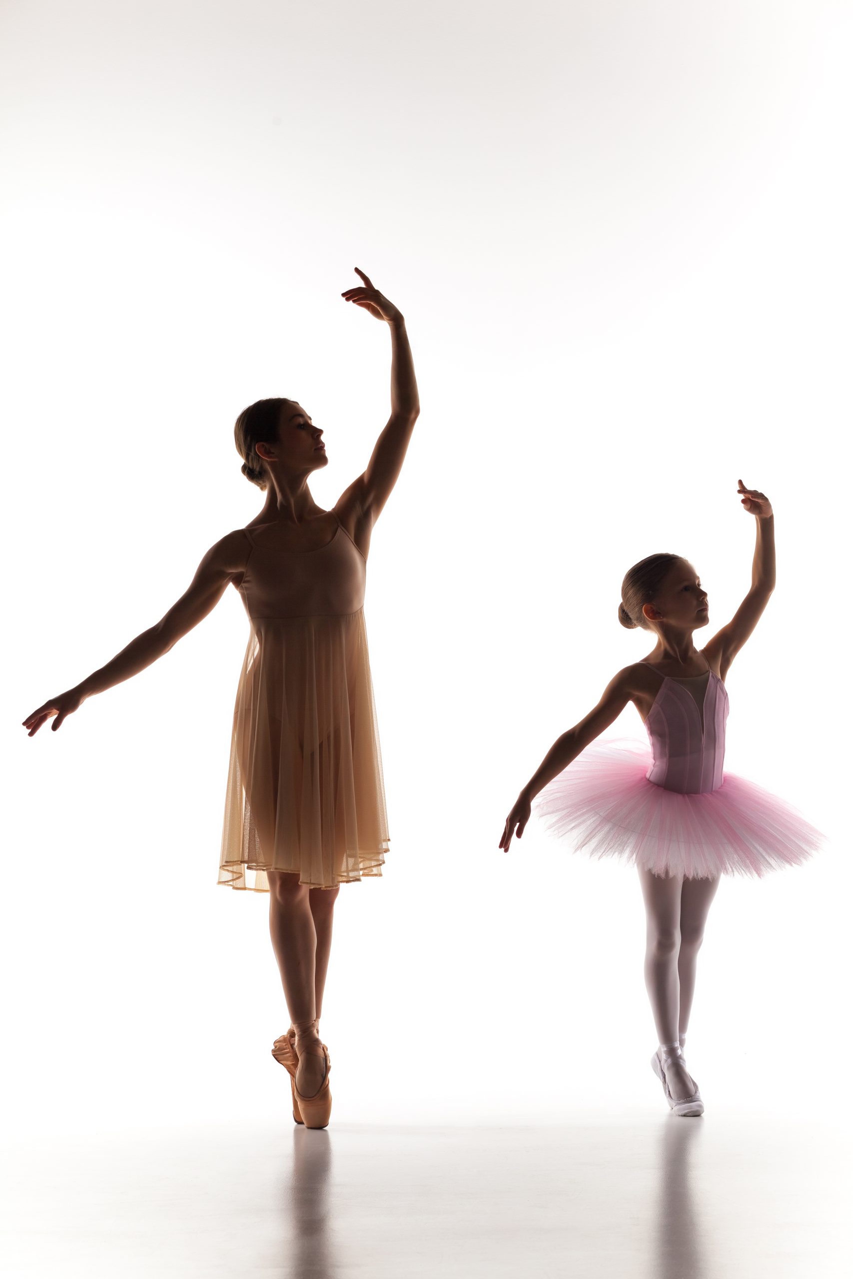The silhouettes of little ballerina and personal classic ballet teacher in dance studio dancing on a white background